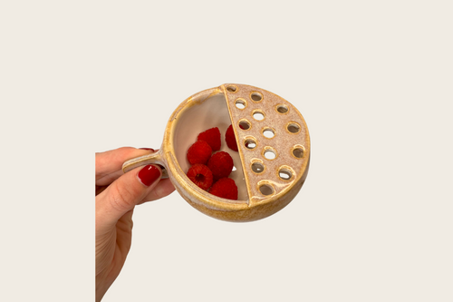 Hand holding a ceramic bowl with half solid and half honeycomb pattern, filled with raspberries.